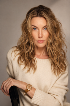 Woman with blonde, wavy hair and blue eyes wearing a cream sweater and watch