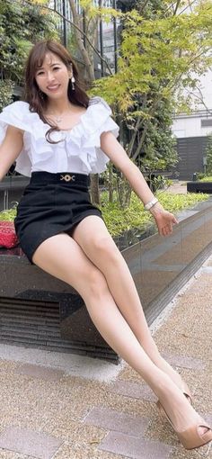 Woman in a white ruffled blouse and black mini skirt sitting outdoors