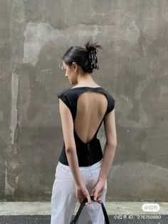 Woman in a black open-back top and white pants against a textured wall