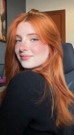 Young woman with long red hair wearing a black top, looking over her shoulder