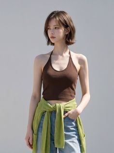 Woman with short hair wearing a brown halter top and jeans with a green sweater