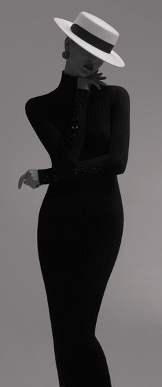 Woman in a black ribbed dress and white hat posing in a studio