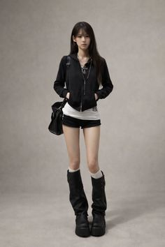 Woman in a black hoodie, short shorts, and platform boots posing in a studio