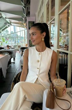 Woman in a white vest with a ponytail sitting in a restaurant with an iced coffee