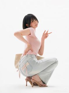 Woman in a pink top and light wash jeans squatting with a peace sign