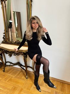 Woman in a black dress and thigh-high stockings posing indoors
