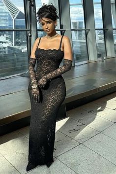 Woman in a black lace dress and long gloves posing indoors with a cityscape view