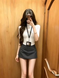 Woman with long hair in a white top and mini skirt taking a mirror selfie