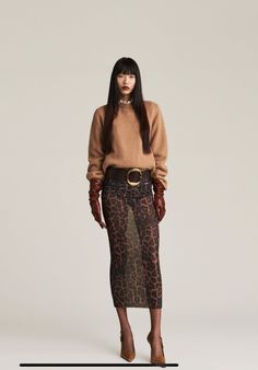 Woman with long black hair wearing a brown sweater and sheer leopard print skirt