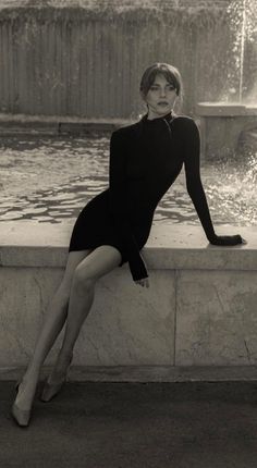 Woman in a black dress sitting by a fountain in black and white