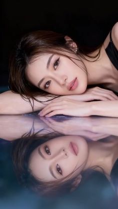 Woman with wet hair and a black top, reflected in water