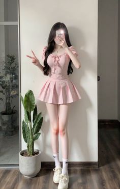 Woman in a pink gingham top and pleated skirt taking a selfie indoors