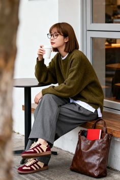 Woman with short hair and glasses sitting outdoors with a coffee cup