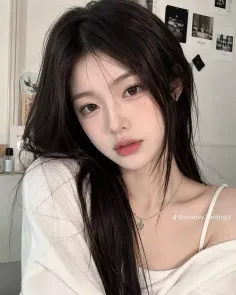 Woman with long black hair wearing a white top and silver necklace indoors