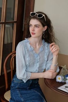 Woman with long hair wearing a blue ruffled blouse and denim skirt indoors