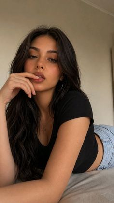 Woman with long dark hair in a black crop top and jeans, lying down
