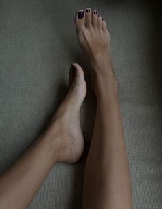 A pair of feet with purple nail polish and legs on a textured surface
