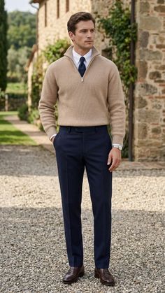 Man in a beige sweater and navy pants standing outdoors on a gravel path