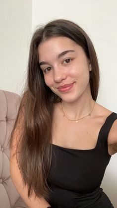 Woman with long brown hair wearing a black top and gold necklace indoors