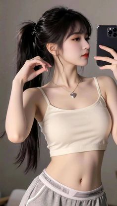 Woman with a ponytail wearing a crop top and heart necklace taking a selfie