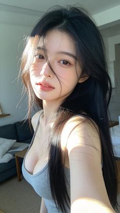 Woman with long black hair in a grey tank top, lit by soft indoor light