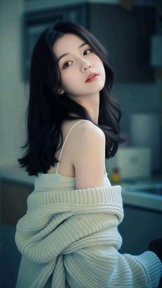 Woman with long black hair wearing a white tank top and knitted sweater