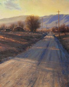 Dirt road leading to farm buildings at sunset with a mountain range in the background