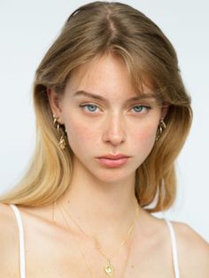 Young woman with blonde hair and blue eyes wearing jewelry against a white background