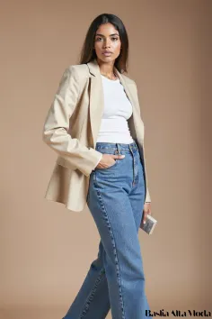 Woman in a beige blazer and blue jeans posing in a studio