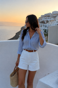 Woman in white shorts and a striped shirt overlooking a coastal town at sunset