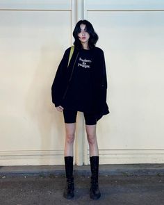 Woman with black hair wearing an oversized sweatshirt, biker shorts, and tall boots