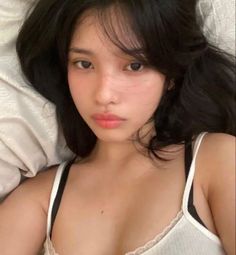 Woman with long black hair wearing a white tank top and black bra