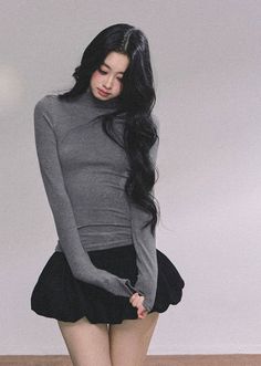 Woman with long black hair wearing a gray turtleneck and black skirt indoors