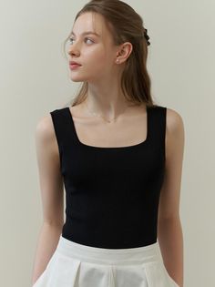 Woman in a black tank top and white skirt looking to the side