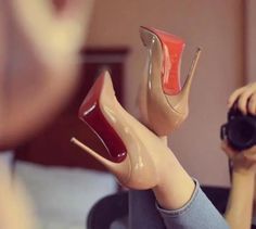 Person wearing nude high heels with red soles and jeans, holding a camera
