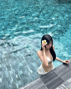 Woman in a white bikini with a frangipani flower in her hair in a swimming pool