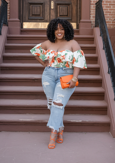 Woman in an off-shoulder floral top and ripped jeans standing on steps