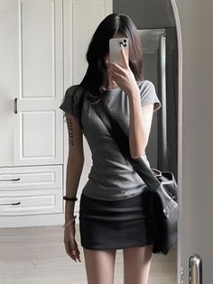 Woman in a gray t-shirt and black mini skirt taking a mirror selfie