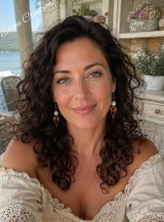 Woman with curly hair and green eyes wearing an off-shoulder top and earrings