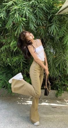 Woman in a white top and khaki pants posing outdoors with green foliage