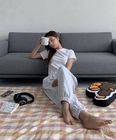 Woman in a white t-shirt and sweatpants sitting on a checkered blanket with a mug