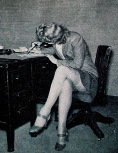 Woman in a suit jacket and stockings writing at a desk