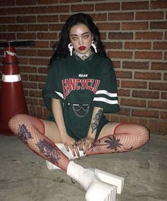 Woman with dark makeup and tattoos wearing red fishnet stockings and an oversized t-shirt