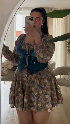 Woman in a floral dress and denim vest taking a mirror selfie