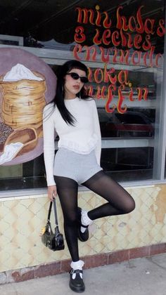 Woman with long black hair and sunglasses posing outdoors in a white top and black tights