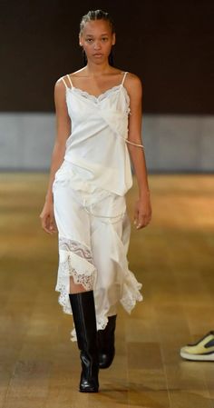 Woman in a white slip dress with lace trim and black boots on a runway