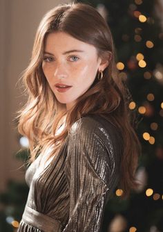 Woman with long hair and freckles in a gold dress with a Christmas tree in the background