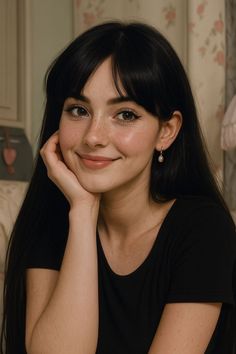 Smiling woman with long black hair and freckles, resting her chin on her hand