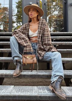 Woman in a plaid shirt, jeans, and cowboy boots sitting on outdoor stairs