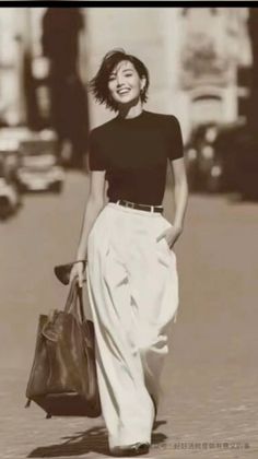 Woman with short hair in a black top and white pants walking on a street